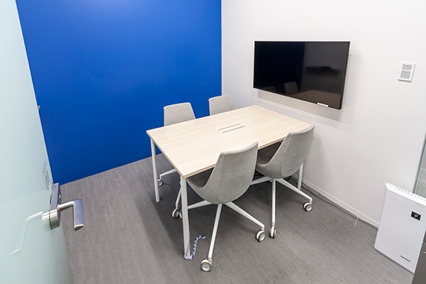 4人用の会議室で、大型モニターと、壁には大型ホワイトボード(画面左側に)。奥の壁は部屋によって変えてあります。こちらはブルーを基調とした部屋です。